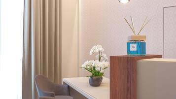 A modern hotel room with a dining area featuring a wooden partition, two pendant lights, a vase with white flowers, and a wooden sideboard.