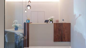 Zona d'estació moderna amb una partició de vidre, taulell de recepció de fusta i una decoració minimalista que inclou un vas amb flors blanques i una petita planta en test.