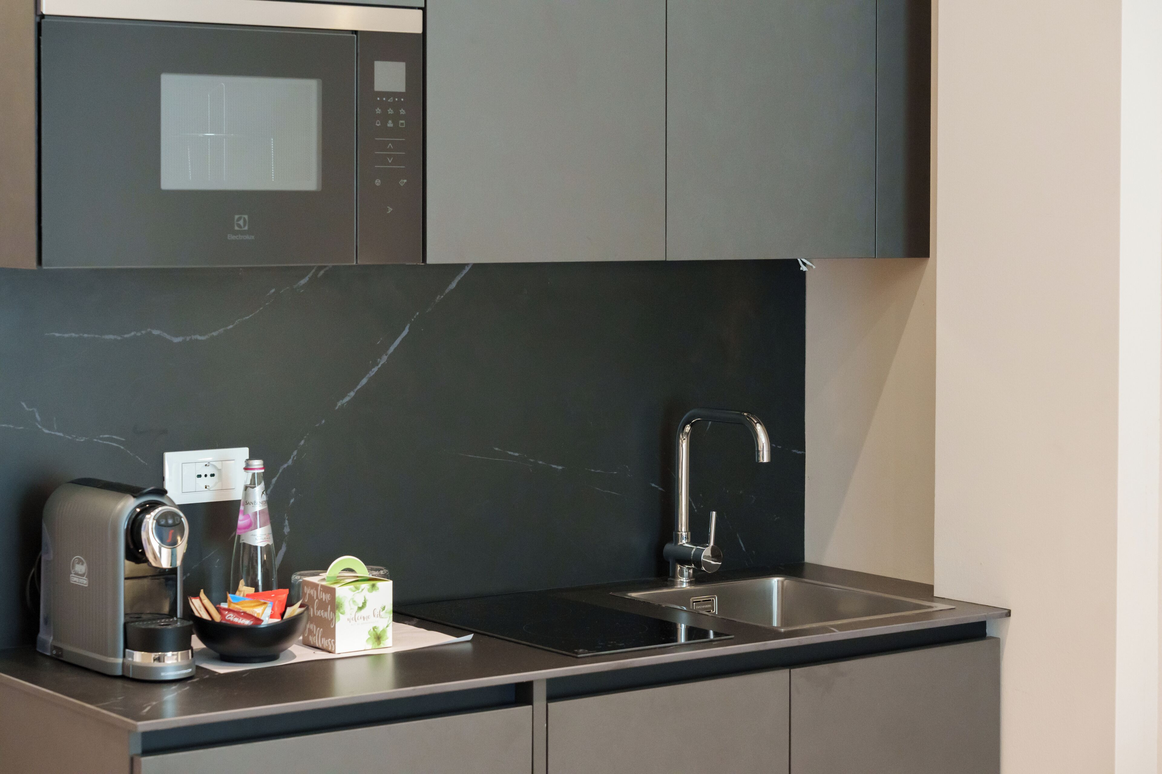 A modern kitchen with a built-in microwave, a coffee maker, a sink, and a marble backsplash.