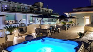 A rooftop patio with a hot tub, outdoor seating, and a view of the city at night. - VI SUITES (Viareggio)