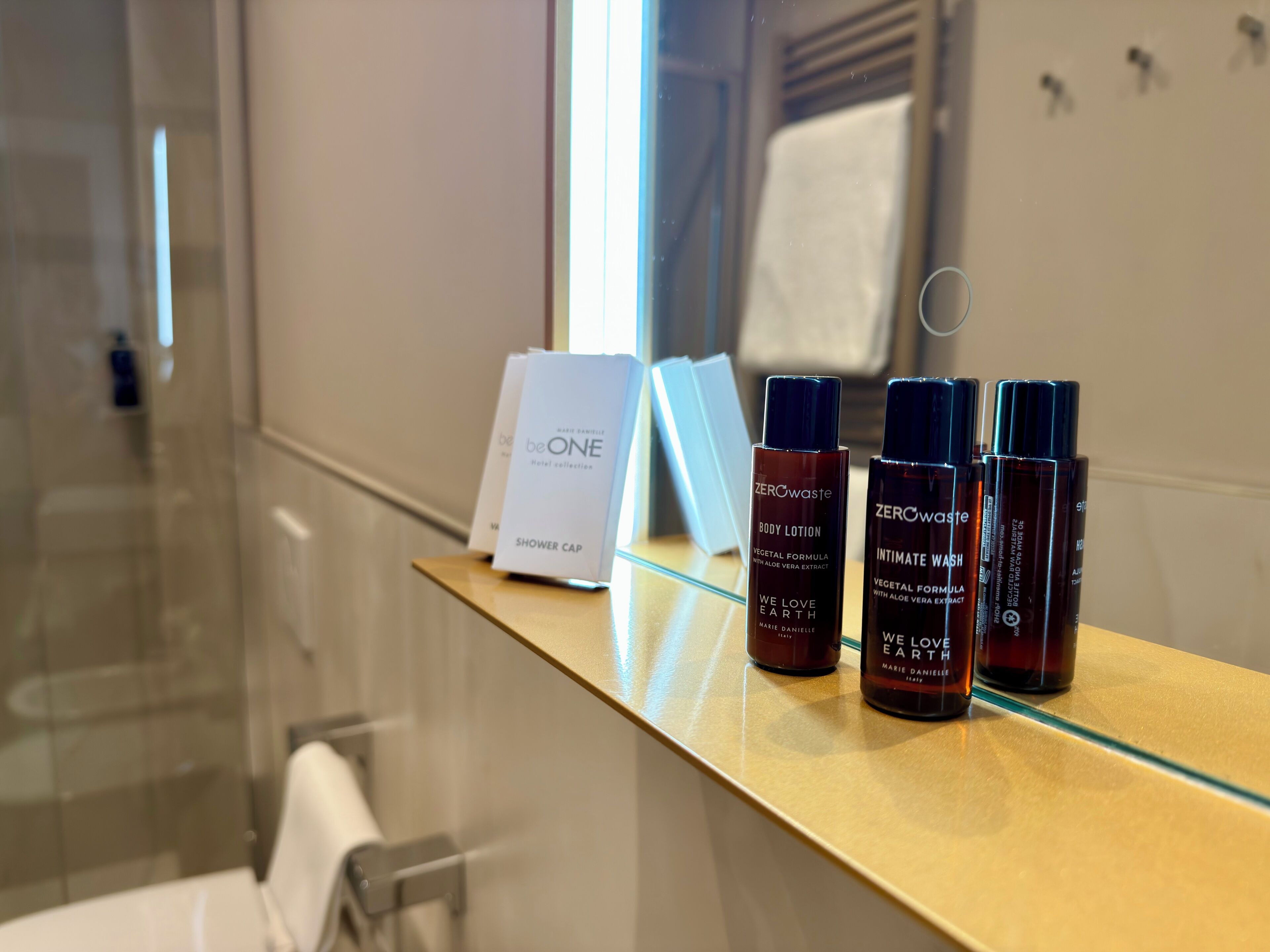A bathroom with a glass shower enclosure, a towel rack, and a shelf with skincare products.