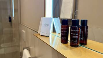A bathroom with a glass shower enclosure, a towel rack, and a shelf with skincare products.