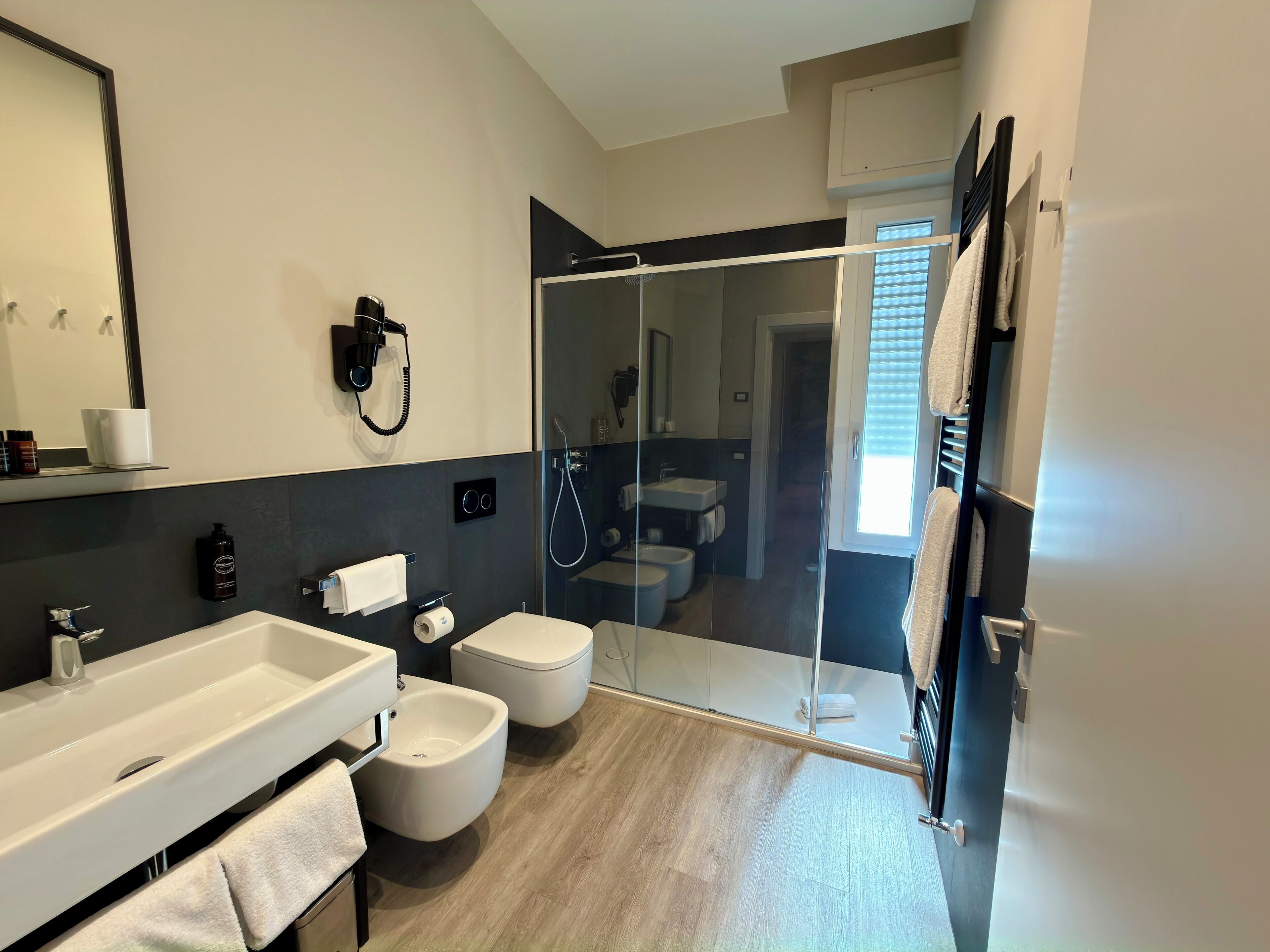 Un baño moderno con un espejo grande, un lavamanos blanco, un bidé y una zona de ducha con mampara de cristal.
