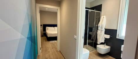 A modern hotel room with a wooden floor, a bed with white linens, a glass shower enclosure, and a white sink.