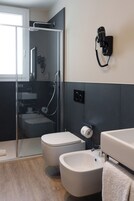 A modern bathroom with a glass-enclosed shower, a toilet, a bidet, and a towel rack.