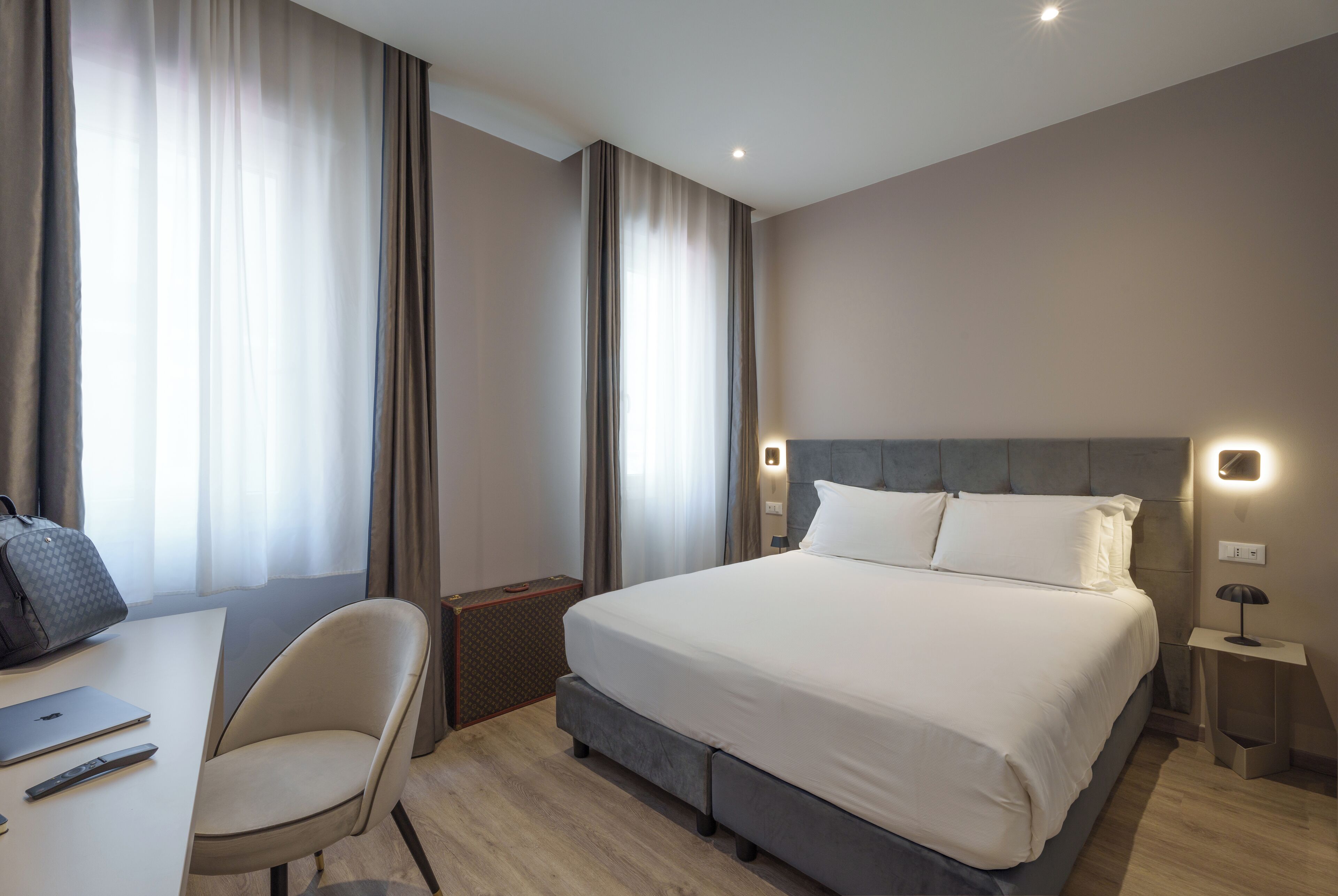 Ein modernes Hotelzimmer mit einem großen Bett, einem Schreibtisch mit einem Laptop, einem Stuhl und einem Koffer.