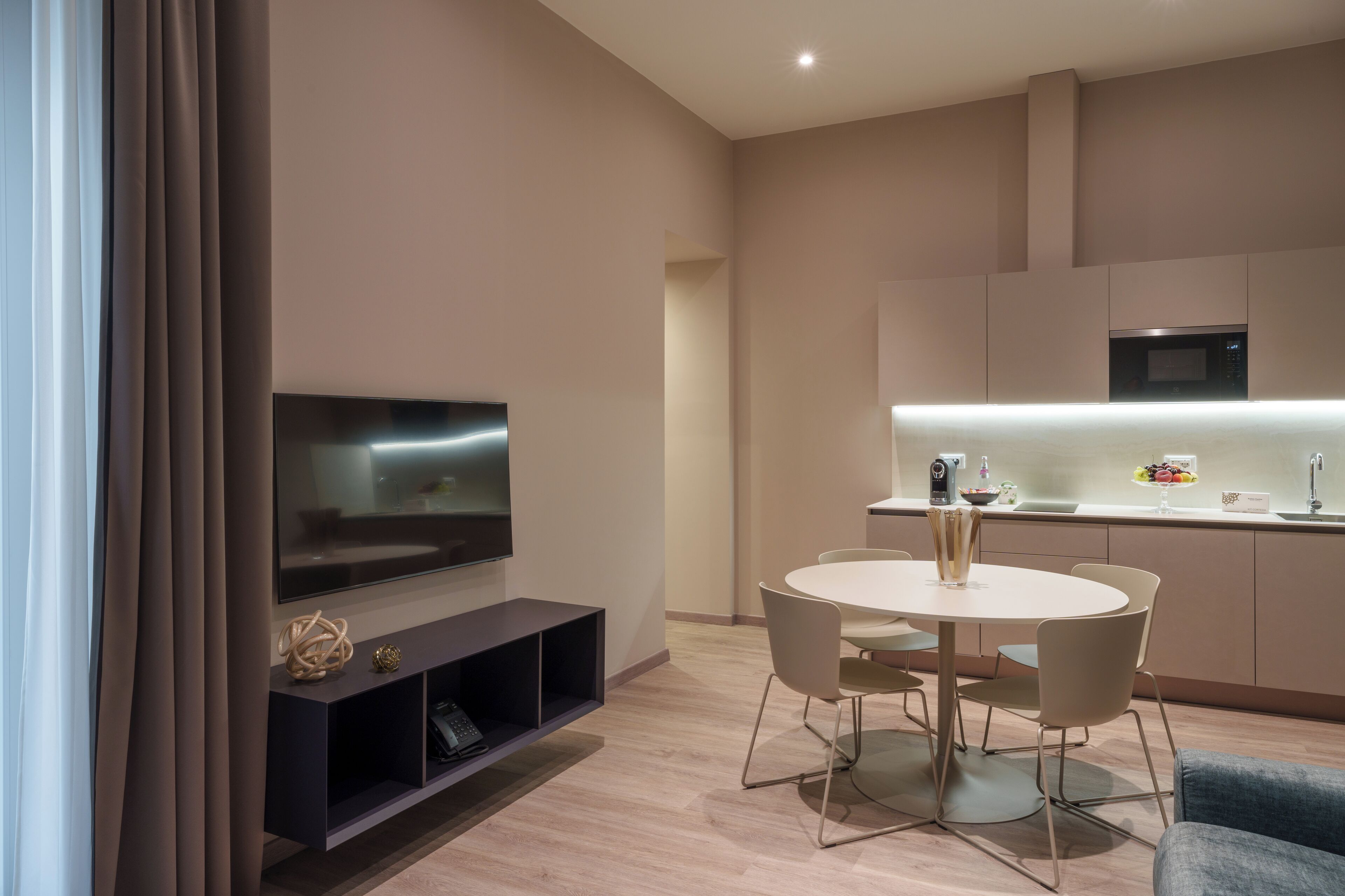 Una sala moderna con televisor de pantalla plana, una mesa de comedor con sillas, un sofá y una zona de cocina con microondas.