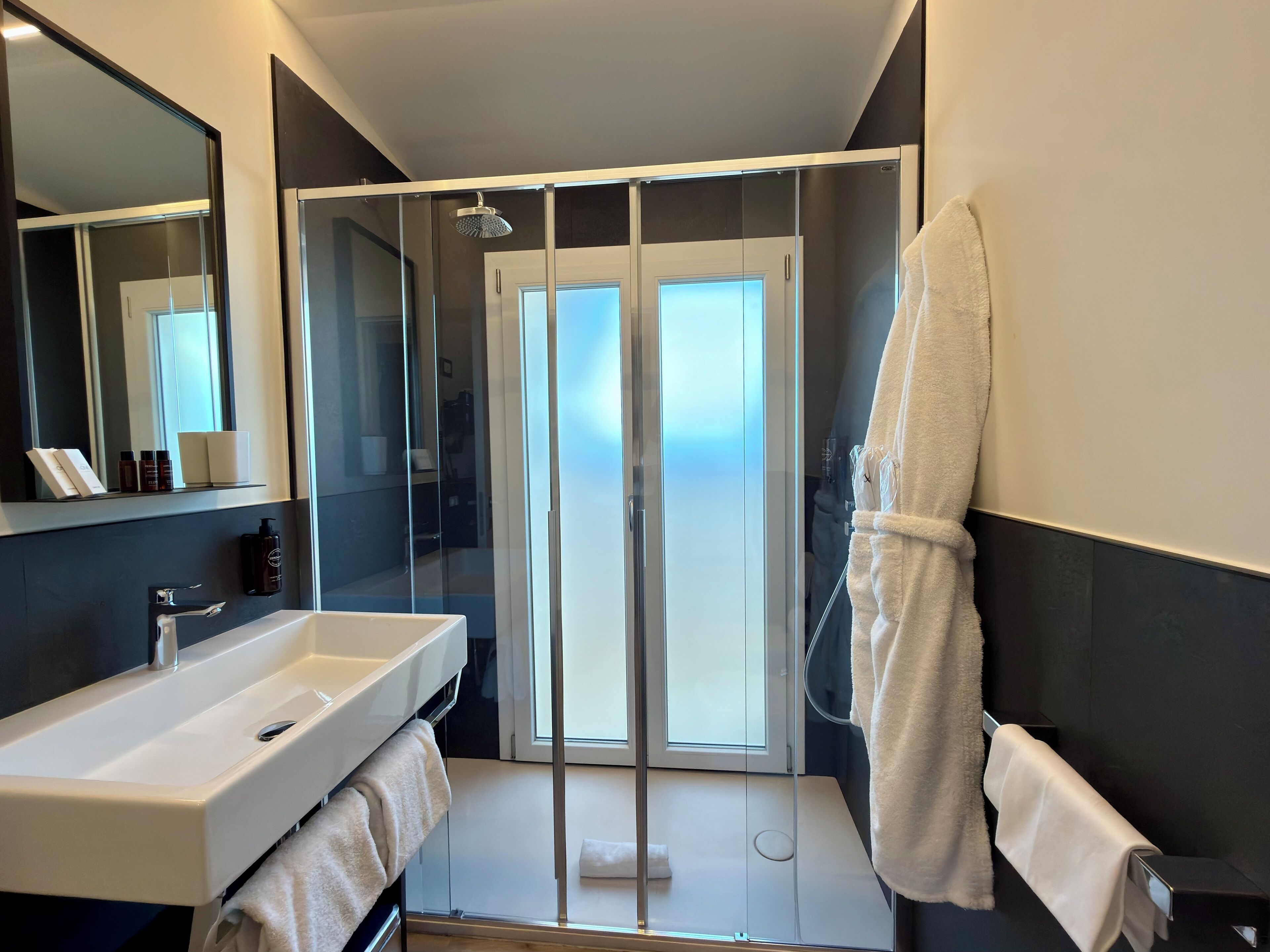 Un baño moderno con cabina de ducha de vidrio, un lavamanos blanco y un espejo grande.