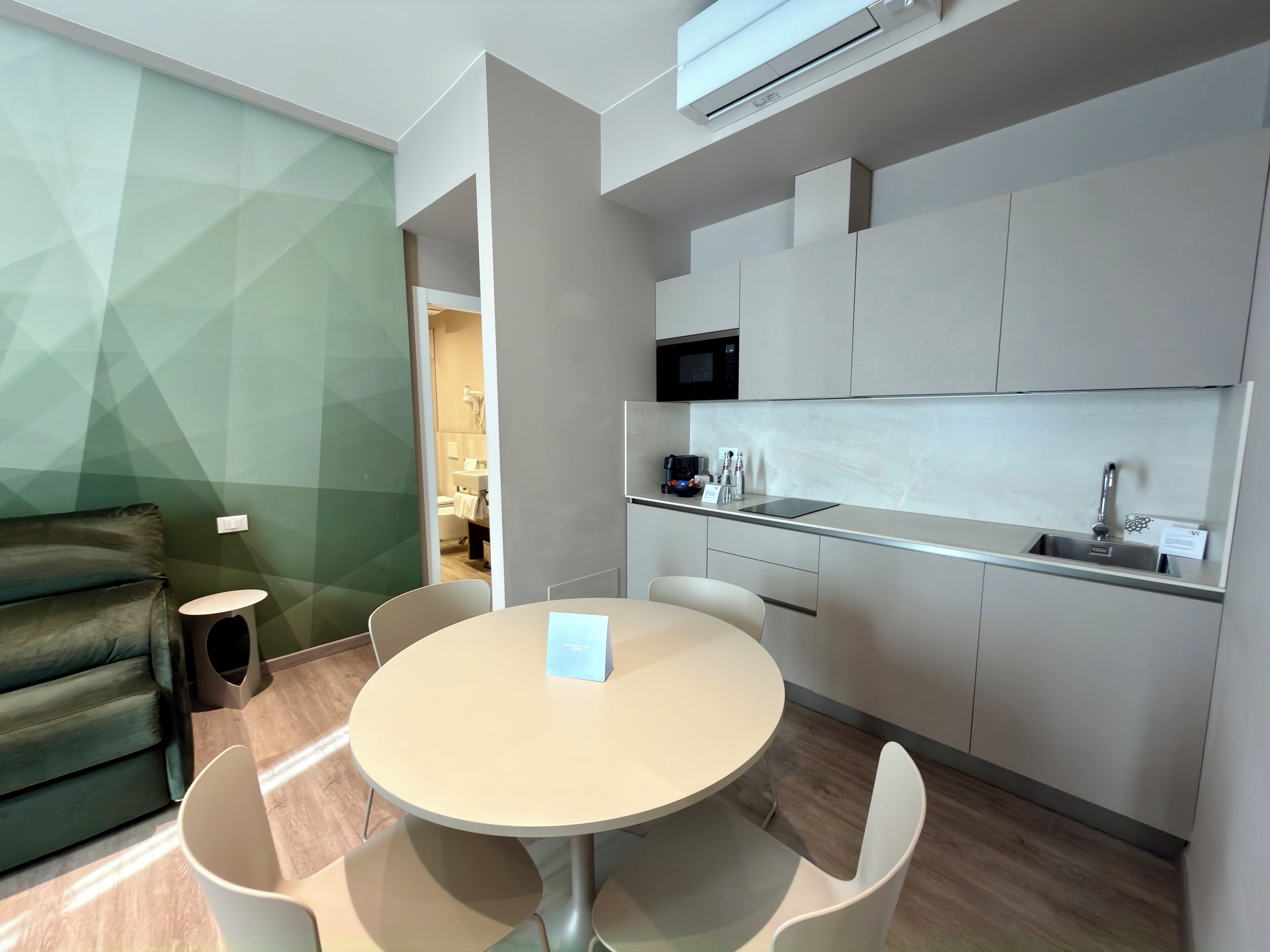 A modern kitchen with a microwave, sink, and coffee maker. There is a dining area with a round table and chairs.