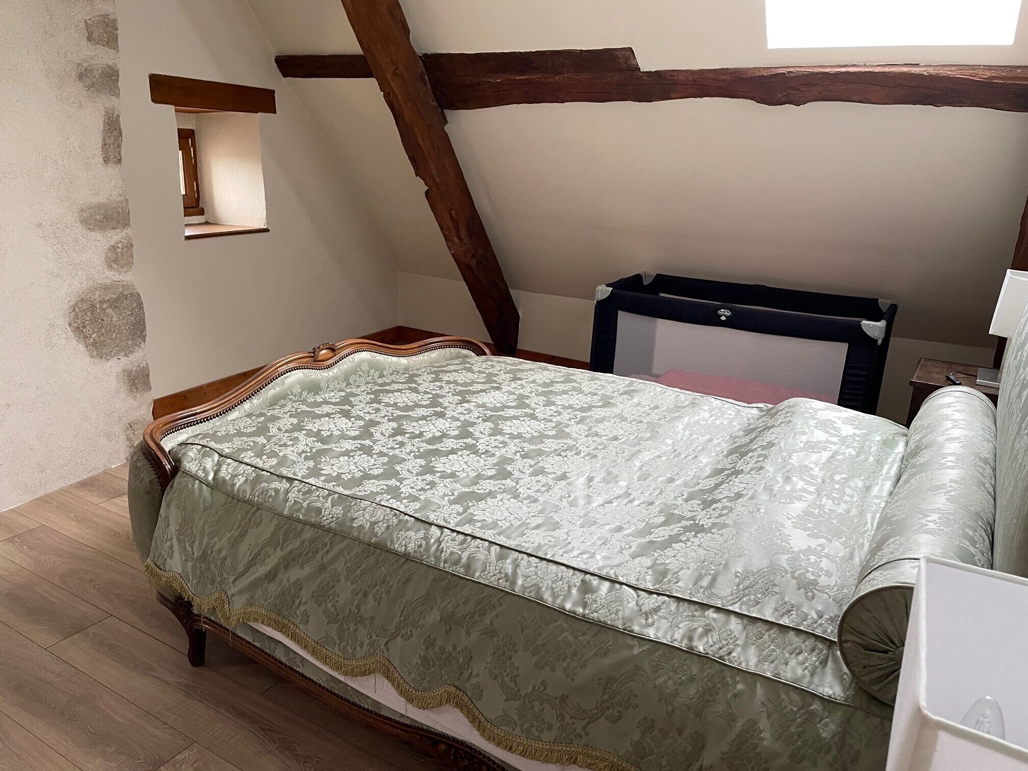 A bedroom with a bed, wooden beams, a stone wall, and a small window.