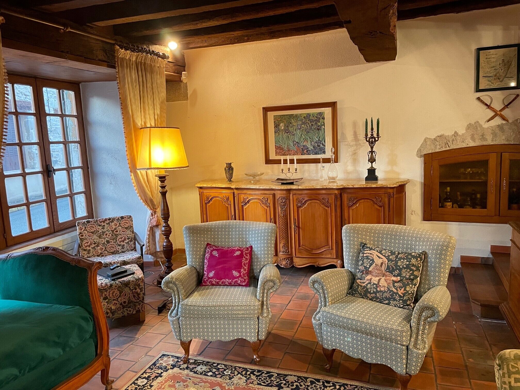 A cozy living room with two patterned armchairs, a green sofa, a wooden cabinet, and a painting on the wall.