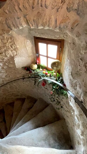 Una escalera de caracol en un edificio de piedra rústica con un ventanal y decoraciones festivas.