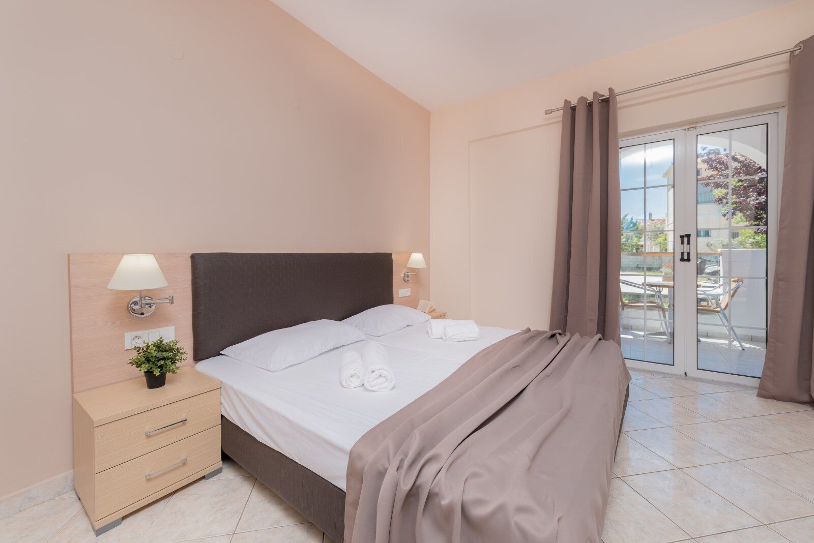 A neatly made bed with white linens, a bedside table with a lamp, and a small potted plant.