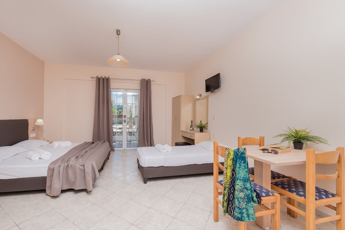 A hotel room with two beds, a desk, a chair, a TV, and a balcony with curtains.