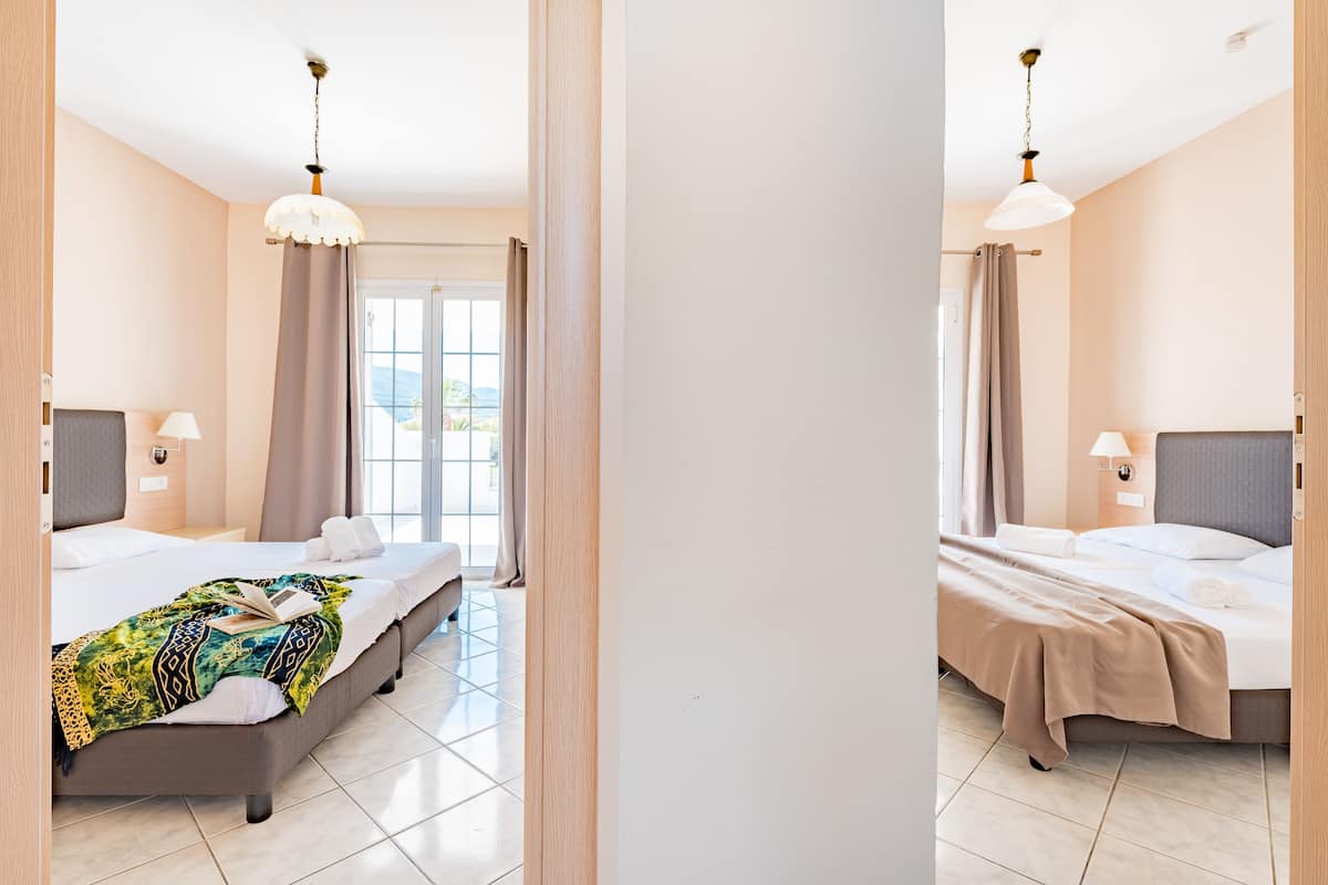 A hotel room with a bed, a bedside table, a lamp, and a view of the outdoors through a window.