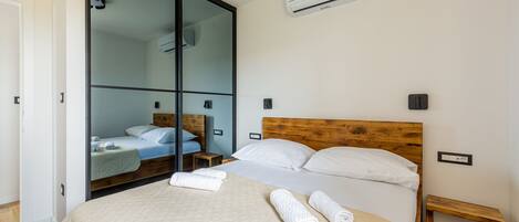 A hotel room with a large sliding door, a bed with a wooden headboard, a bedside table, and an air conditioning unit on the wall.