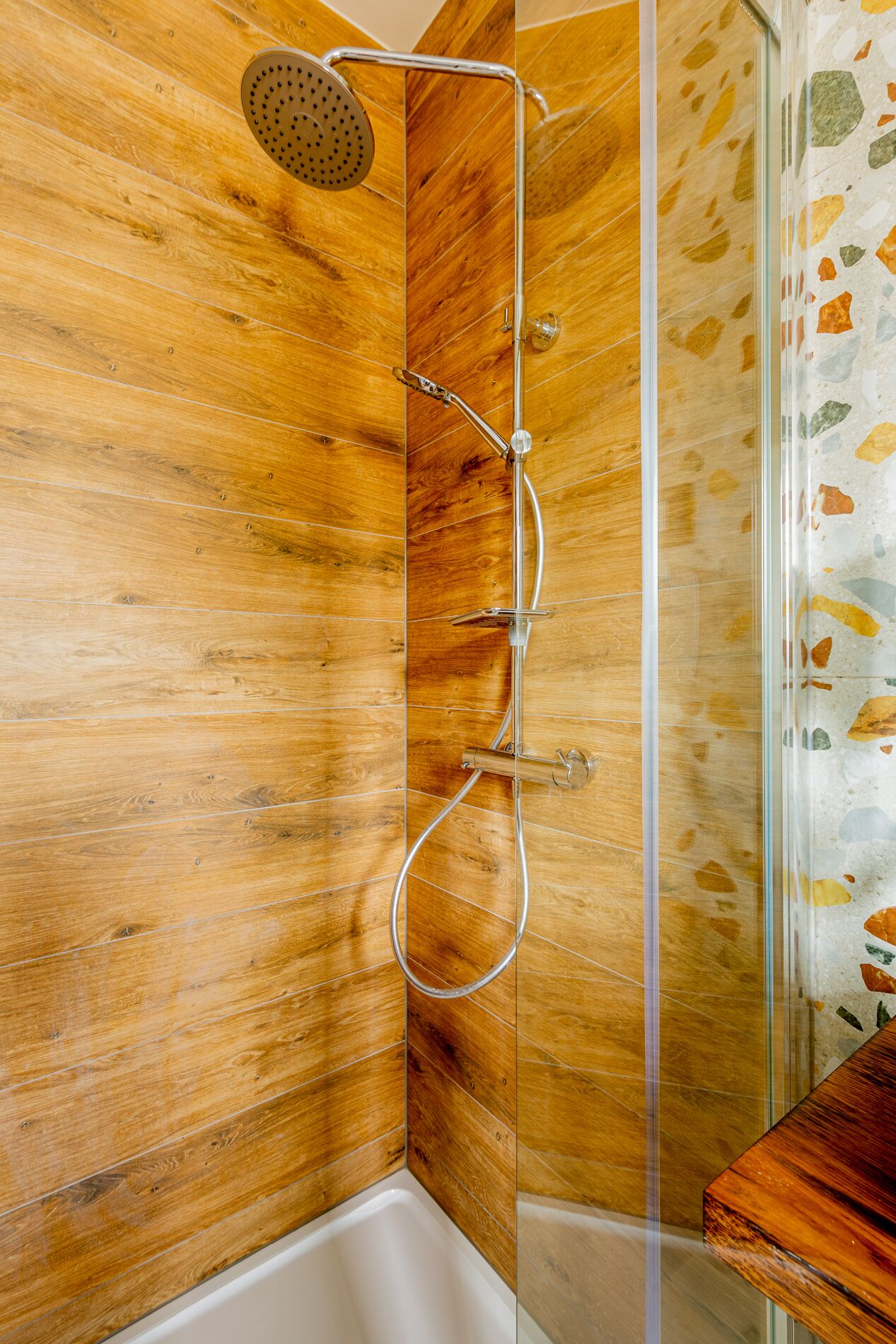 Douche met regenstortdouche en handdouche, houten wand en glazen douchecabine.