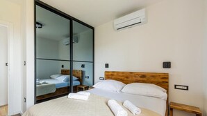 Une chambre d’hôtel avec un lit, une tête de lit en bois, une petite table de chevet en bois, une serviette sur le lit et une porte coulissante donnant sur une autre pièce.
