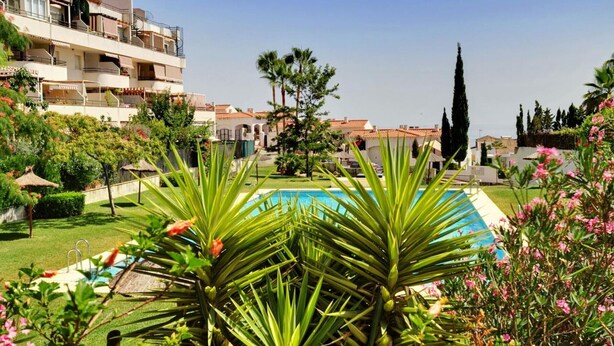 A pool area with a clear view of a building with balconies and a garden with palm trees and flowers. - Quiet apartment between golf and sea with pool (Rincón de la Victoria)