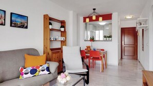 A modern living room with a sofa, coffee table, and a dining area with red chairs and a wooden cabinet. - Quiet apartment between golf and sea with pool (Rincón de la Victoria)