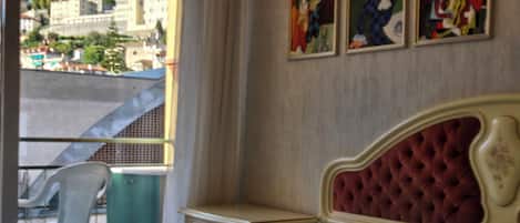 Un dormitorio con cama, una silla, una mesita de noche y una ventana con vista a edificios.