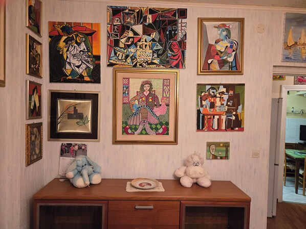 Une pièce avec un bureau en bois, divers tableaux encadrés accrochés au mur et un jouet en peluche posé sur le bureau.