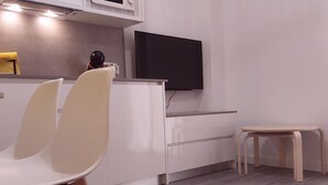 A modern kitchen with white cabinetry, a built-in microwave, and a flat-screen TV mounted above the counter. There are two white chairs and a small wooden stool. - Large central apartment in Malaga for 4, ideal for family or couple (Málaga)