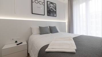 Habitació d'hotel moderna amb un llit ben fet, una tauleta de nit amb un comandament a distància i una petita planta.