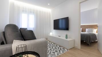 Een moderne, goed verlichte woonkamer met een grijze bank, een flatscreen televisie en een minimalistisch design.