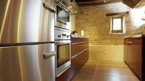 Una cocina con refrigerador de acero inoxidable, dos hornos, armarios de madera y una pared de piedra.