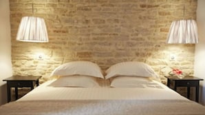 Un dormitorio con pared de piedra, una cama con ropa blanca, dos mesitas de noche y dos lámparas.