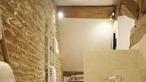 Un baño rústico con pared de piedra, vigas de madera, una bañera y un banco de madera.