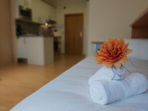Siististi pedattu sänky, jonka päällä on rullattu valkoinen pyyhe ja suuri oranssi kukka.