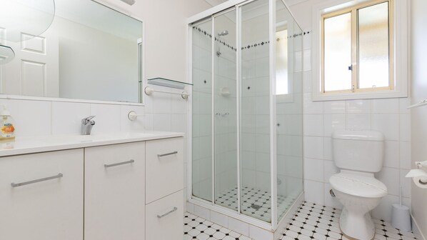 A bathroom with a glass-enclosed shower, a toilet, and a sink with a mirror above it. - Private Infinity Pool Sleeps 8 Near One Mile Beach (Forster)