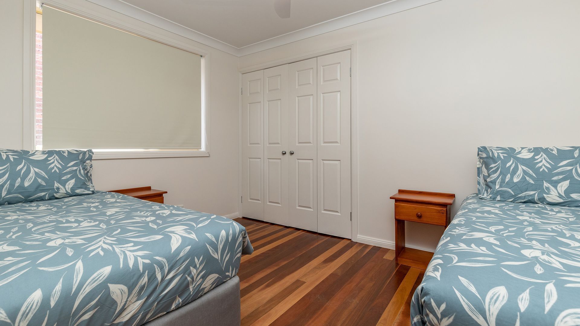 A bedroom with two beds, a window, a wardrobe, and a wooden floor.