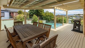 Un espacio exterior techado con una mesa y sillas de madera, una parrilla y una piscina.