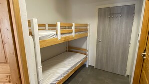 Une petite pièce compacte, avec un lit superposé, une porte et un sol carrelé.