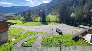 Un espace de stationnement avec une voiture, entouré d’herbe verte et d’arbres, avec des montagnes en arrière-plan.