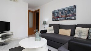Uma sala de estar moderna com televisão de tela plana, um sofá cinza, uma mesa de centro branca e uma pintura com vista para a cidade na parede.
