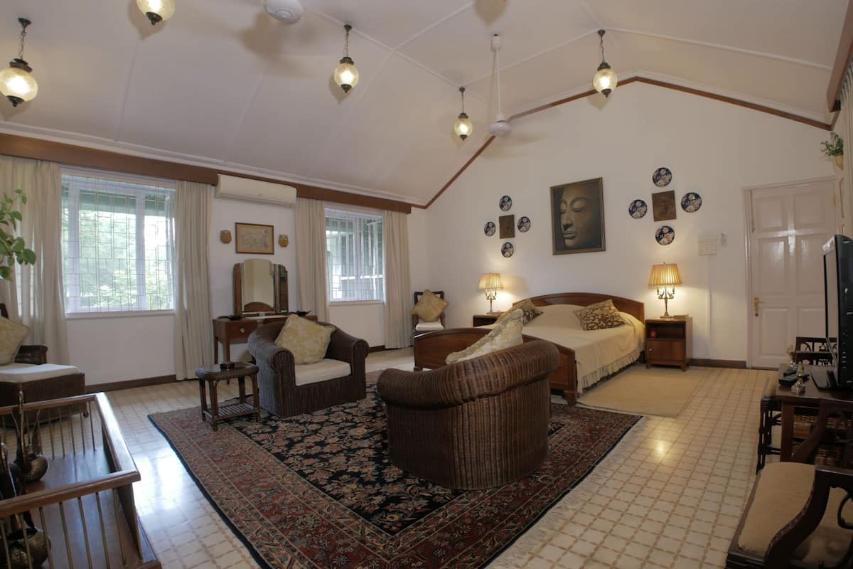 A spacious living room with a large bed, two sofas, a coffee table, and a dining table. There are multiple wall decorations and a large window with curtains.