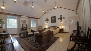 A spacious living room with a large bed, two sofas, a coffee table, and a dining table. There are multiple wall decorations and a large window with curtains.