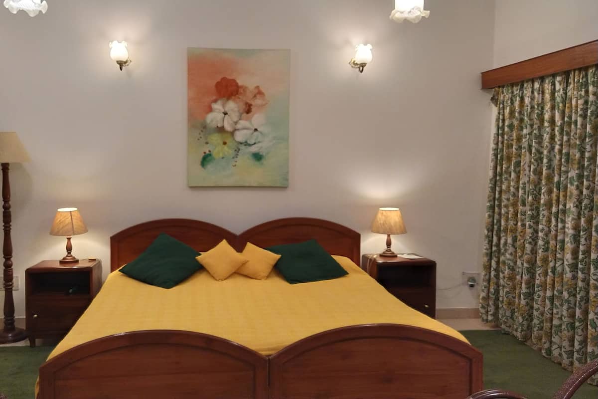 A bedroom with a wooden bed, floral curtains, two bedside lamps, and a painting on the wall.