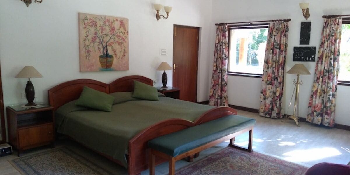 Une chambre à coucher avec un lit, des lampes de chevet, une table de chevet, un banc, une fenêtre avec des rideaux et un tableau au mur.