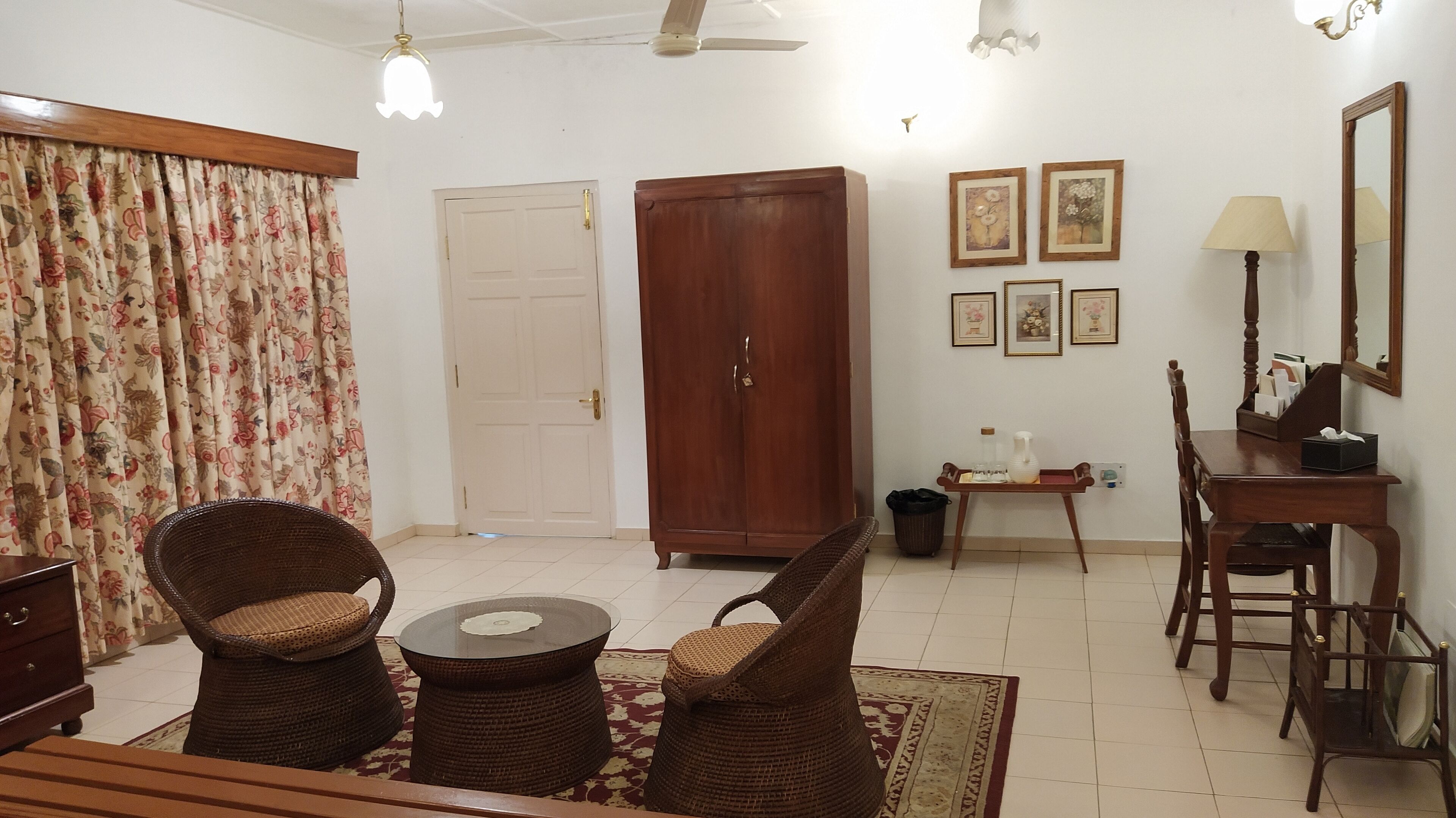 A living room with wicker furniture, a wooden cabinet, a table with a vase, and framed pictures on the wall.