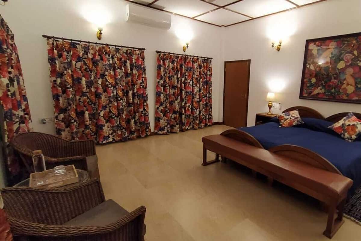 A bedroom with a bed, a bench, a chair, a nightstand, a lamp, and a painting on the wall.