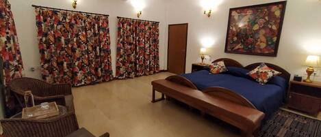 A bedroom with a bed, a bench, a chair, a nightstand, a lamp, and a painting on the wall.