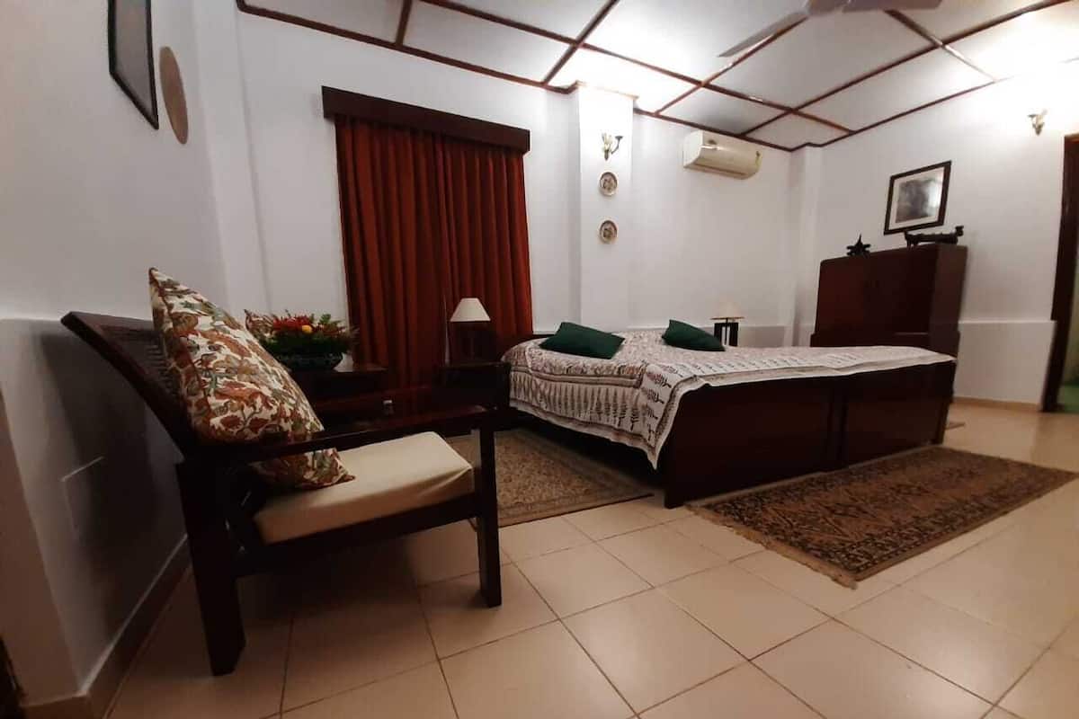 A bedroom with a bed, a chair, a dresser, and a window with curtains.