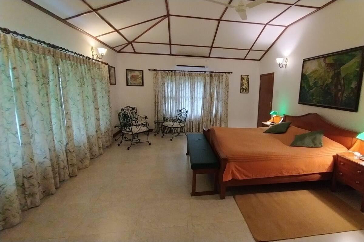A bedroom with a bed, bedside tables with lamps, a bench, a chair, and a painting on the wall.