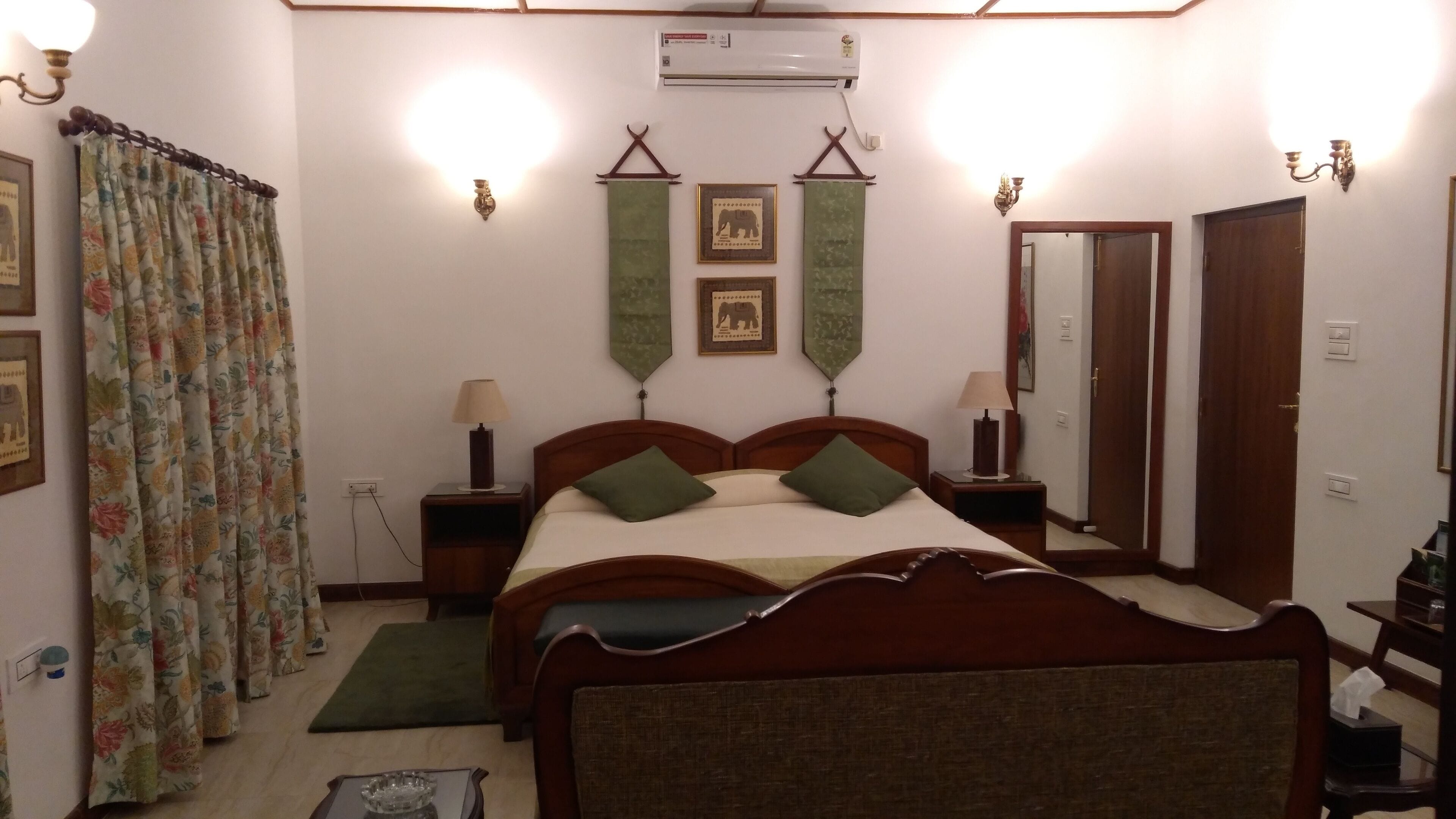 A hotel room with a wooden bed, two bedside tables with lamps, a green rug, a mirror, and two wall-mounted light fixtures.