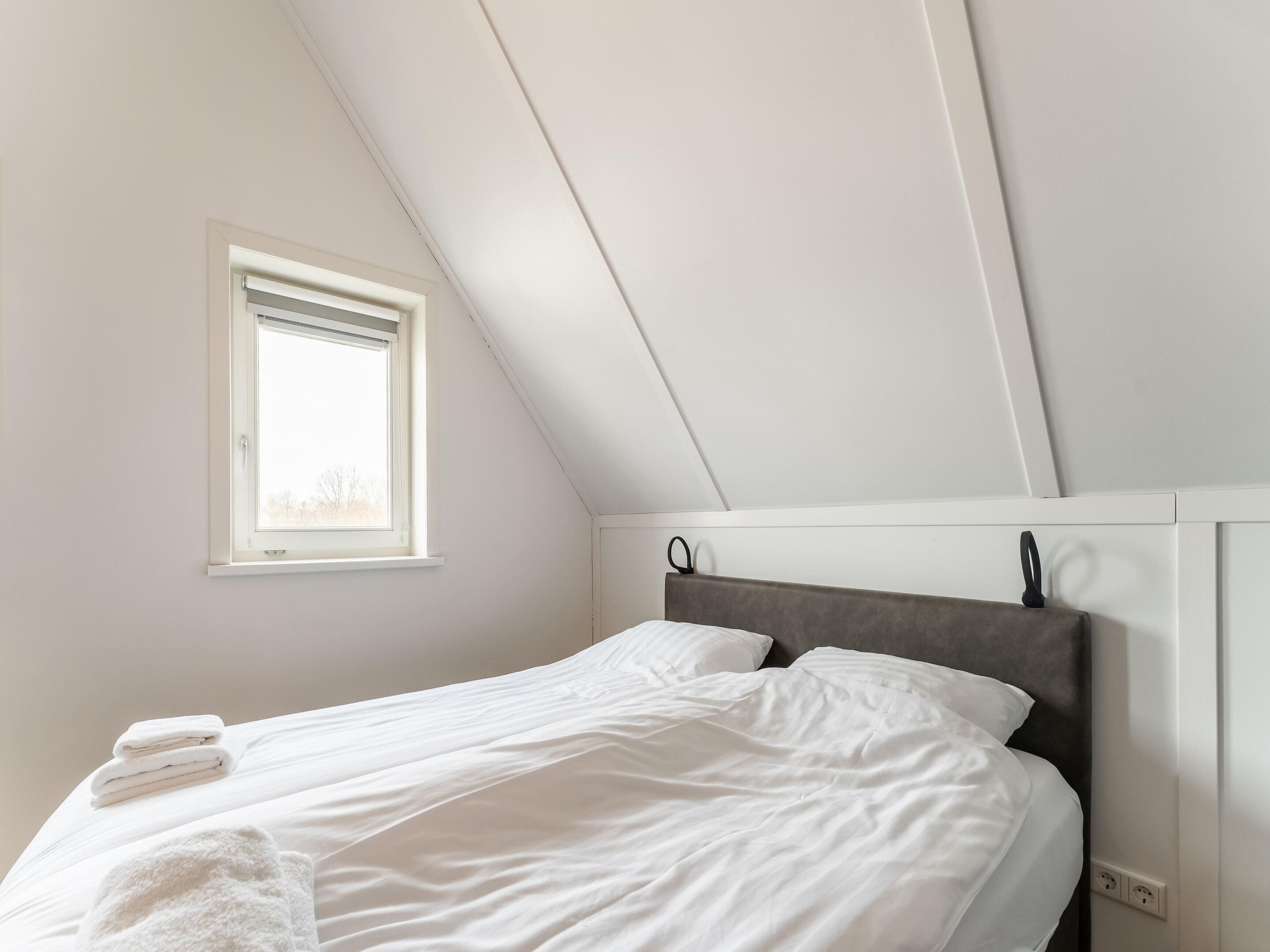A bedroom with a bed, a window, and a sloped ceiling.